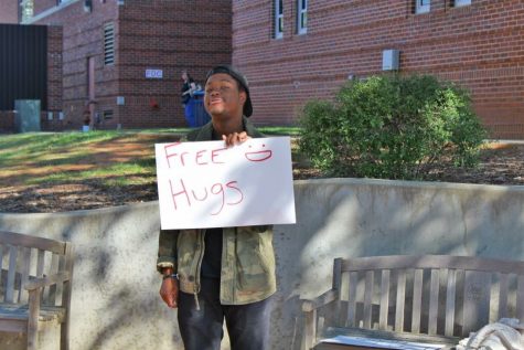 Student, Ralontae Worley, standing outside the Fine Arts building offering free hugs to passing students. 