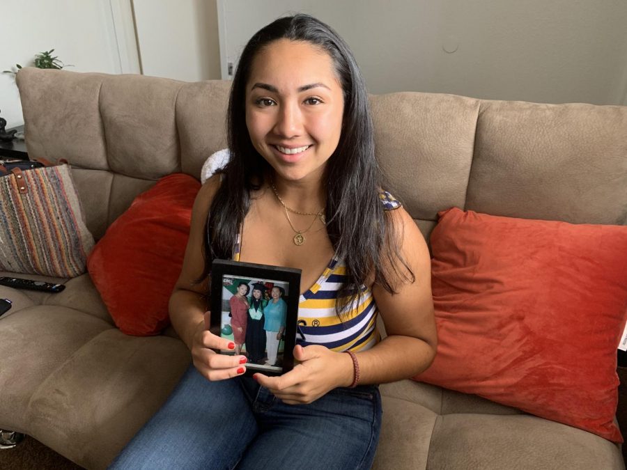 Nicole Maldonado poses with a photo from her high school graduation. In the photo she stands with her arms wrapped around her mother and grandmother, whom she has not seen in two years.